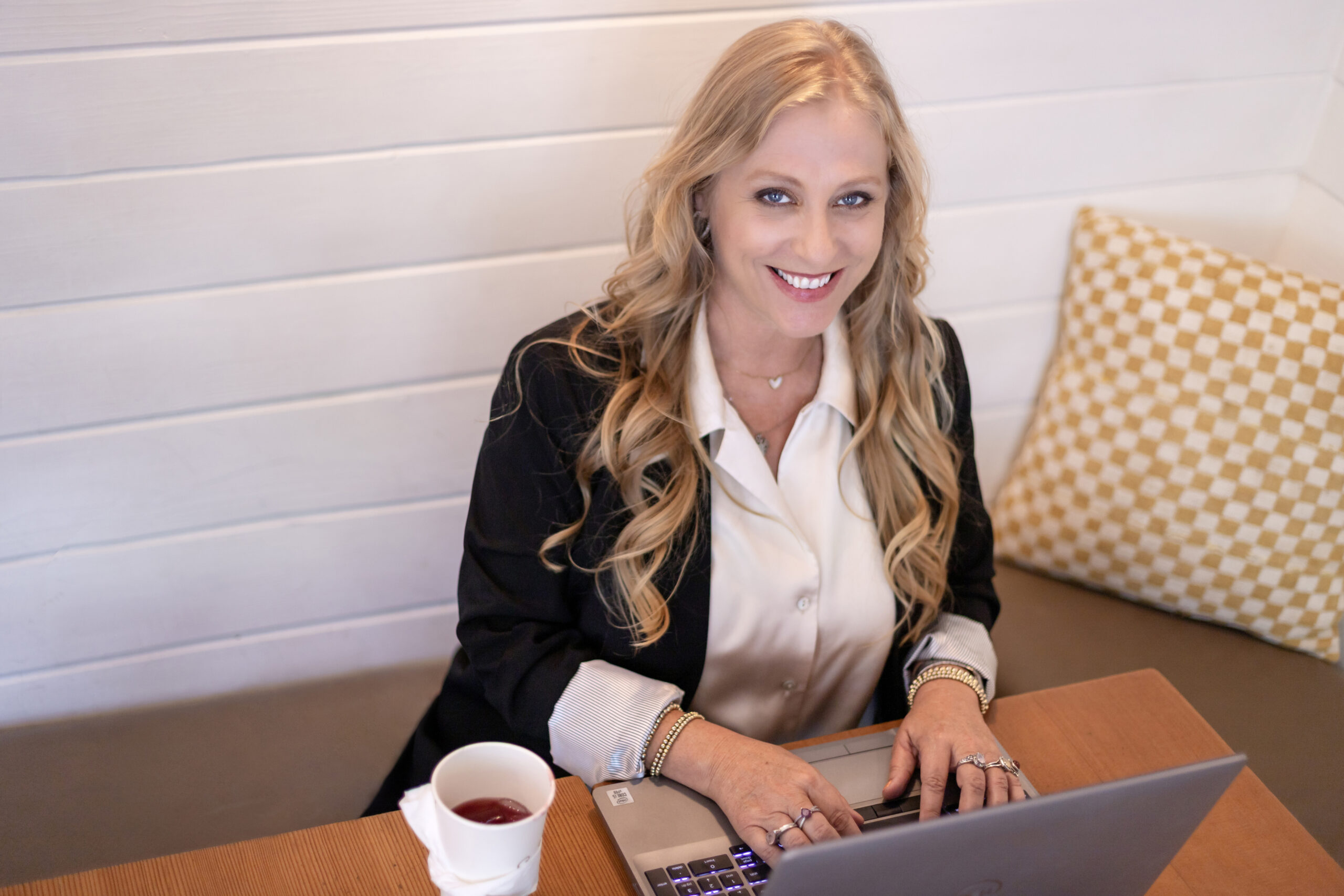 Julianne-D_6117 Julianne, a dedicated Medicare Insurance Advocate, smiles while working on her laptop at a cozy café table — helping clients navigate their Medicare options with care and expertise.